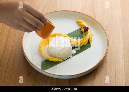 Avant de déguster du riz collant à la mangue, il est essentiel de le arroser de lait de coco pour ajouter une légère salinité, qui complète la douceur du R. Banque D'Images