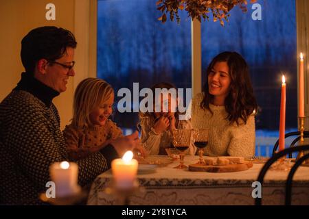 Famille profitant d'un dîner aux chandelles ensemble, souriant et partageant un moment de joie autour d'une table. Banque D'Images