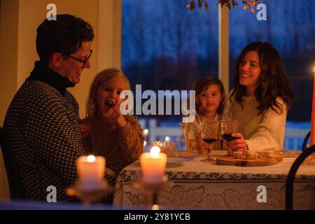 Famille appréciant un dîner aux chandelles confortable avec des sourires et des rires. Banque D'Images