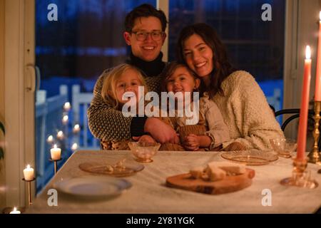 Une famille de quatre appréciant un dîner aux chandelles confortable avec des sourires chaleureux autour de la table. Banque D'Images