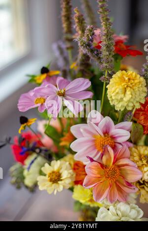 Un bouquet vibrant de fleurs mélangées comprenant du cosmos, des zinnias et de la lavande affiché près d'une fenêtre. Banque D'Images