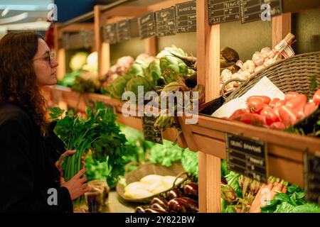 Femme magasinant des légumes dans une épicerie, sélectionnant soigneusement les produits d'un affichage bien approvisionné. Banque D'Images