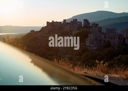 La lumière tôt le matin baigne un village de pierre abandonné avec un fond de collines ondulantes et un lac calme. Banque D'Images