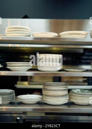 Piles de plaques blanches organisées sur étagères métalliques dans une cuisine professionnelle. Banque D'Images