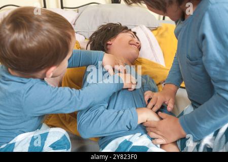 Trois enfants en pyjama jouent ensemble et se chatouillent au lit. Scène légère et ludique. Banque D'Images