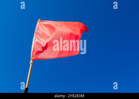 Avertissement drapeau rouge agite sur vent fort au-dessus du ciel bleu sur la plage Banque D'Images