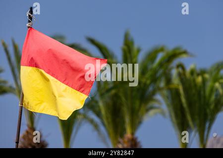 Drapeau d'avertissement rouge et jaune est monté sur la plage, les palmiers sont sur le fond flou Banque D'Images