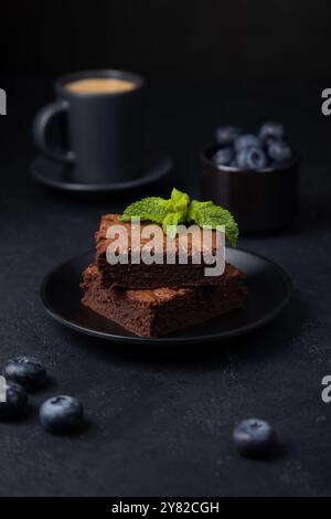 Gâteau au brownie au chocolat avec menthe, myrtilles et expresso. Dessert américain traditionnel. Gâteau populaire au chocolat noir sur fond noir. Clos Banque D'Images