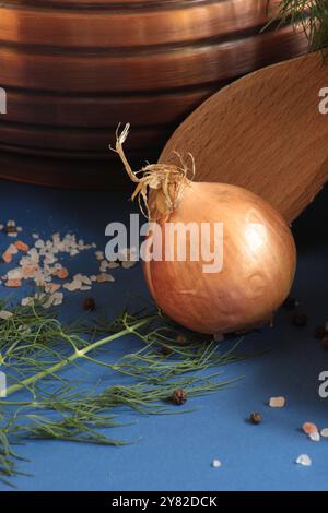 Oignon entier avec grains de sel, cuillère en bois et bol en cuivre, disposés sur un fond bleu foncé pour une composition rustique, de mauvaise humeur et élégante Banque D'Images