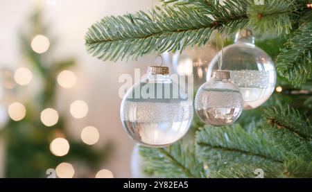 Boules de Noël en verre suspendues sur des branches de pin vert avec des lumières festives, ornements de Noël brillants avec fond bokeh, élégant minimaliste Banque D'Images