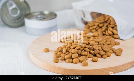 Une planche à découper en bois avec de la nourriture pour animaux dispersée dessus, à côté d'un sac ouvert de croquettes. En arrière-plan, il y a une boîte de nourriture humide pour animaux de compagnie. Le paramètre est Banque D'Images