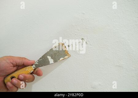 Gros plan de la main masculine du travailleur tenant la spatule et grattant la vieille peinture. Banque D'Images