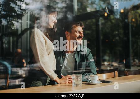 Deux amis partagent des rires et des boissons chaudes dans un charmant café, créant une atmosphère accueillante qui célèbre la connexion et la joie pendant une journée ensoleillée Banque D'Images