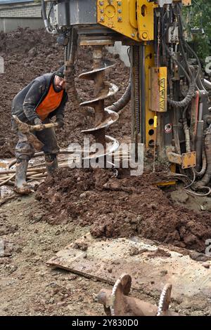 Nettoyage manuel des déblais de la machine de forage de pieux de tarière perçant un trou dans un sol argileux sur un chantier de construction domestique Banque D'Images