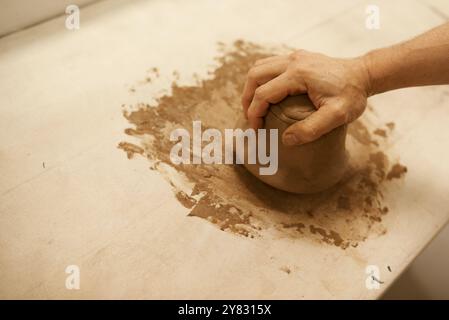 Gros plan d'un potier masculin façonnant un morceau d'argile humide tout en travaillant à une table dans un atelier de céramique Banque D'Images