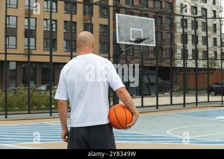 Joueur de basket-ball avec ballon de basket-ball orange sur la cour du terrain de sport. Panier de basket-ball. Vue arrière. Parc public urbain à l'extérieur. Banque D'Images