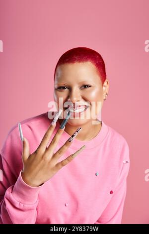 Une jeune femme confiante avec les cheveux roses et piercing nez affiche joyeusement son style frappant dans un studio. Banque D'Images