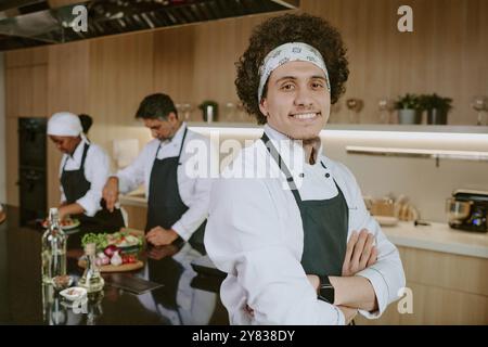 Portrait moyen en gros plan d'un jeune sous-chef aux cheveux bouclés souriant largement tout en posant pour la photo Banque D'Images