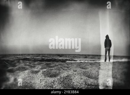 Image créative texturée lourde d'un soldat debout sur une plage vide regardant au-dessus de l'eau. Banque D'Images