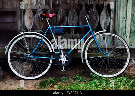 Un vieux vélo bleu, se dresse devant une maison en bois vintage. Banque D'Images