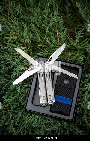 Couteau de poche MultiTool dans un étui ouvert sur verdure. Banque D'Images