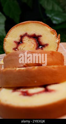 Tranches de gâteau roulées sucrées sur tapis de bambou avec des feuilles d'érable, fougères et décorations de feuillage Banque D'Images