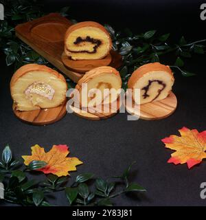 Quatre tranches molles de gâteau roulé avec différentes garnitures, allant de la confiture de fruits à la crème de noix, servies sur des planches de bois avec un fond de feuille verte Banque D'Images