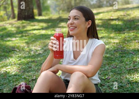 Jeune étudiante assise détendue buvant du jus de détox rouge avec de l'orange de betterave et de la carotte dans le campus universitaire Banque D'Images