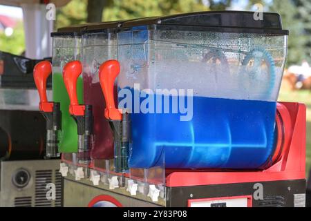 Machine à slush faisant des boissons glacées colorées avec différentes saveurs, boissons rafraîchissantes avec de la glace en bleu, rouge et vert à un marché funfair, sélectionné Banque D'Images