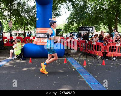 Un coureur masculin de semi-marathon franchissant la ligne d'arrivée avec le chronomètre de la course en vue. Banque D'Images