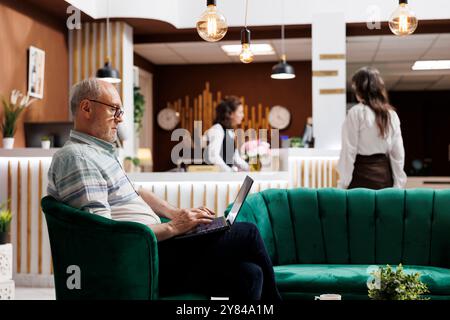 Les clients de sexe féminin s'enregistrent à la réception de l'hôtel pendant que les touristes de sexe masculin naviguent et réservent leur chambre à l'aide d'un ordinateur portable. Homme âgé retraité utilisant son ordinateur personnel pour l'enregistrement en ligne. Banque D'Images