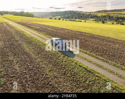 Une voiture noire roule le long d'une voie de campagne, entourée de vastes champs sous un ciel nuageux, Carsharing, VW ID5, Calw, Forêt Noire, Allemagne, Europe Banque D'Images