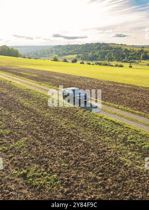 Voiture noire conduisant sur une voie de campagne gravillonnée à travers un large paysage rural sous un ciel nuageux, Carsharing, VW ID5, Calw, Forêt Noire, Allemagne, EUR Banque D'Images