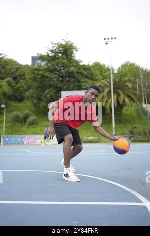 Photo verticale pleine longueur d'un adolescent africain joueur de basket-ball dribble dans un court extérieur Banque D'Images