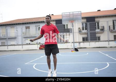 Photo horizontale pleine longueur d'un jeune sportif africain à la corde à sauter dans une installation de basket-ball en plein air Banque D'Images