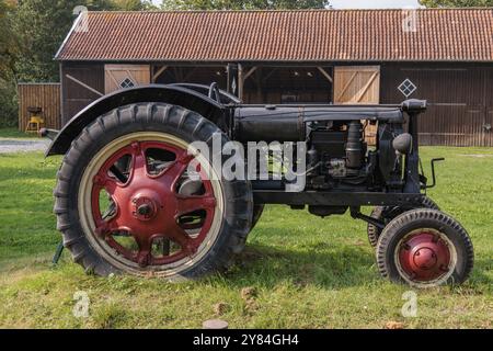 Vieux tracteur rouge debout sur l'herbe verte devant une grange en bois, krummhoern, frise orientale, allemagne Banque D'Images