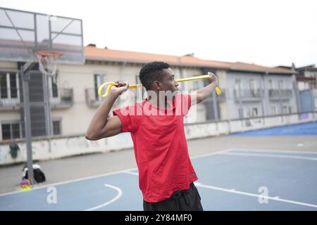 Garçon africain athlétique s'étirant à l'aide d'une bande élastique dans un terrain urbain de basket-ball extérieur Banque D'Images