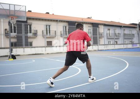 Vue arrière d'un jeune afro-américain méconnaissable jouant au basket-ball en plein air sur un terrain urbain Banque D'Images