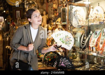 Une femme souriante qui inspecte les fans orientaux de la boutique d'antiquités Banque D'Images