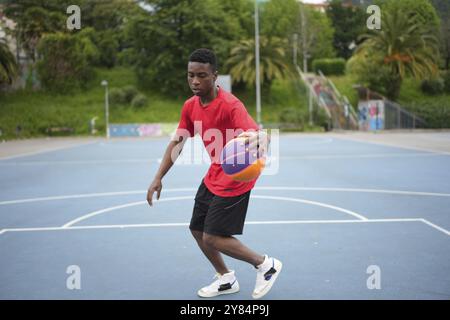 Jeune homme africain jouant au basket seul dans un parc avec des installations Banque D'Images