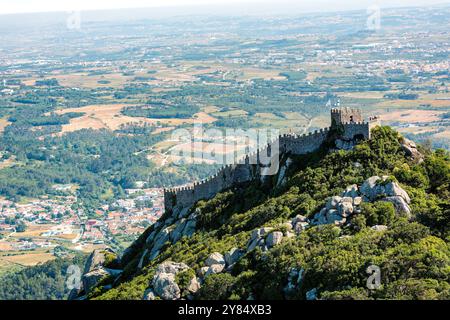 Château mauresque murs de pierre Sintra Portugal // SINTRA, Portugal — le château mauresque (Castelo dos Mouros) se dresse bien en vue sur une colline au-dessus de la ville de Sintra. Cette forteresse médiévale, avec ses murs de pierre serpentant le long de la ligne de crête, offre une silhouette spectaculaire contre le ciel et offre une vue imprenable sur le paysage environnant. Banque D'Images