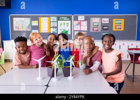 À l'école, groupe d'enfants divers souriant autour de la table avec des éoliennes Banque D'Images