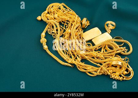 Beaucoup de colliers d'or et de lingots d'or sur fond de tissu de velours vert. Banque D'Images