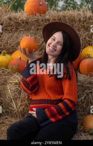 Portrait d'une femme tenant une citrouille assise sur des balles de foin Banque D'Images