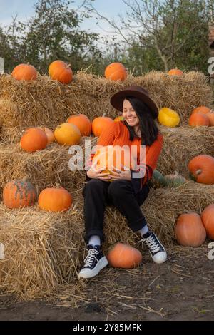 Portrait d'une femme tenant une citrouille assise sur des balles de foin Banque D'Images