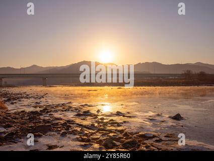 Un matin d'hiver serein près du 5e pont de Soyang à Chuncheon, Corée du Sud, le 2022 février. Le lever du soleil jette une lueur dorée sur la scène paisible. Banque D'Images