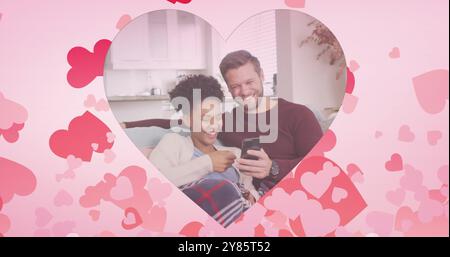 Image de cœurs sur un couple diversifié à l'aide d'un smartphone sur un canapé Banque D'Images
