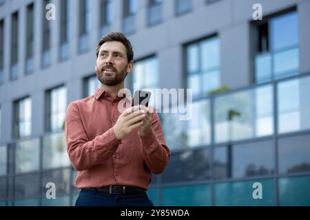 Un homme en chemise rouge tient un téléphone portable. Il sourit. Banque D'Images