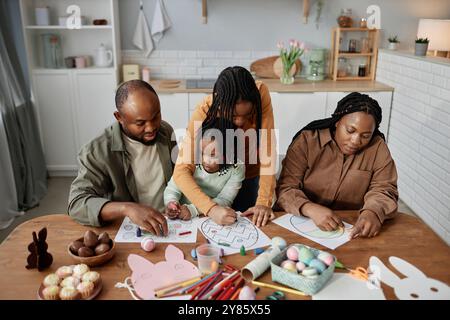 Famille s'engageant dans les arts et l'artisanat à table de cuisine avec des activités sur le thème de Pâques. Parents et enfants travaillant ensemble avec des jouets et des décorations Banque D'Images