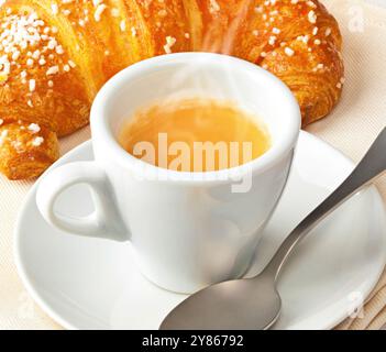 Une tasse de café à la vapeur est posée sur une soucoupe avec un croissant frais, prêt à être dégusté pour le petit déjeuner Banque D'Images